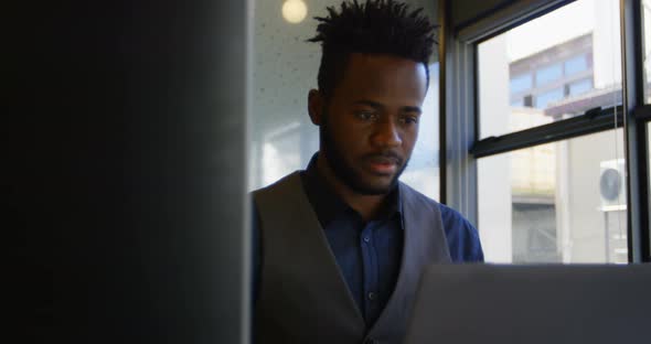 Front view of young black businessman working on laptop at desk in a modern office 4k