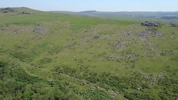 Wide shot aerial tracking forwards towards several tors scattered throughout the shot. Dartmoor, Eng