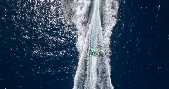 Aerial drone view of man and woman on an inflatable tube towing behind a boat to a tropical island.