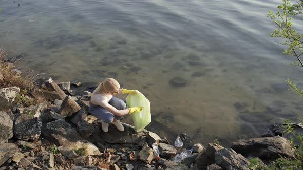 A Woman Removes Rubbish Among the Stones Near the Lake