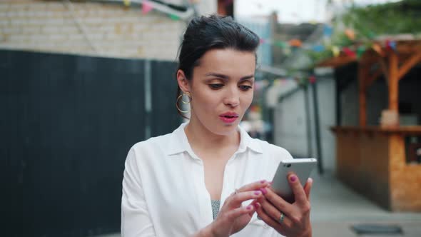 Excited Adult Woman Looking at Smartphone Outdoors After Getting Great News