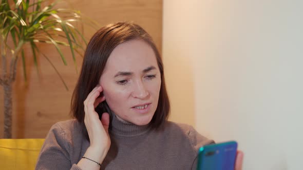 Happy Woman Sits in a Chair and Chats on Social Networks Using Mobile Phone Smartphone