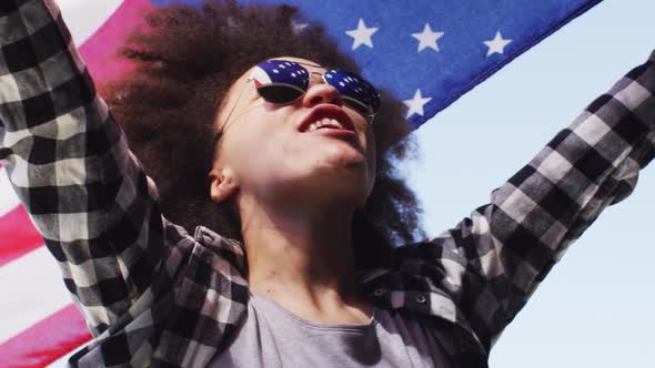 African american woman wearing sunglasses holding american flag up in the air