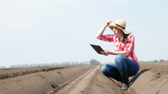 Female Farmer, Agronomist Sits Between Special Soil Rows on Field. She Tests, Using Tablet, Quality