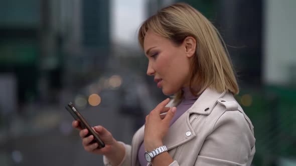 Portrait of a Beautiful Blonde Middle-aged Woman Typing on a Mobile Phone Outdoors in the City.