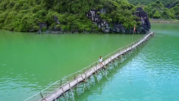 Upper View Blond Girl Walks on Old Bridge To Rocky Island