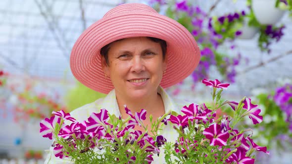 Happy Elderly Woman Florist Stand in Greenhouse Holding a Pot of Flowers in Hands