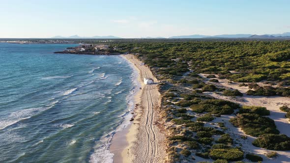 Trench Beach on Mallorca Island in Spain with people walking near a tent on the sand, Aerial flyover