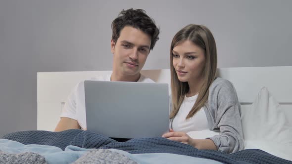 Happy Young Couple Using Laptop in Bed