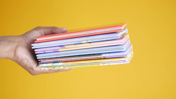 Hand Holding Stack of Books on Color Background