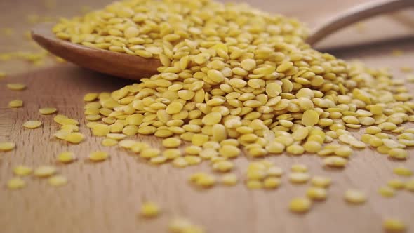 A full wooden spoon of yellow raw lentils. Falling and pouring of asian legumes