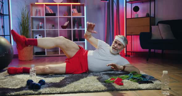 Old Bearded Man in Sportswear Doing Leg Stretching Exercises Lying on the Floor