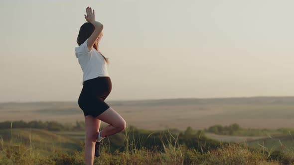 Pregnant woman stands outdoor in yoga pose, performing daily workout, side view. Pregnant woman