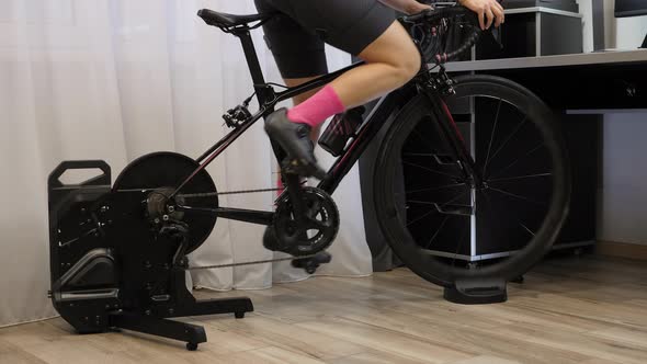 Woman is pedaling out of saddle on indoor smart bicycle trainer.