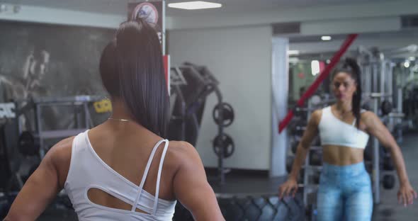 Female fitness trainer flexing her muscles and body in front a mirror at the gym