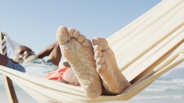 Happy senior african american man lying in hammock on sunny beach
