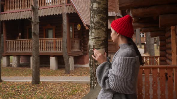 Woman in a Knitted Red Hat and Scarf Drinks Hot Tea Standing