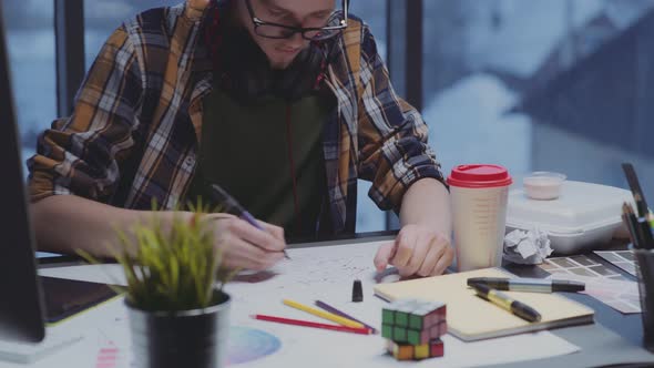 Modern Designer with Headphones Makes Sketches in Front of Window