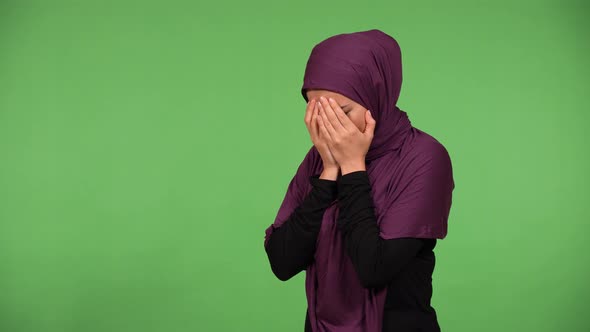 A Young Beautiful Muslim Woman Cries with Hands Covering Her Face  Green Screen Background