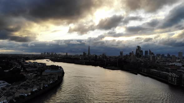 Flying over river Thames as the dramatic stormy dark, clouds gather over London skyline at sunset