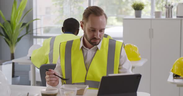 Construction Company Worker in Reflective Vest Having Lunch and Using Digital Tablet in Canteen