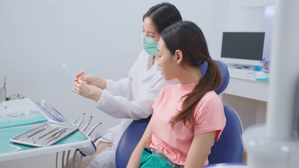 Asian young girl listening female dentist explain about oral care and teeth brush in dental clinic.