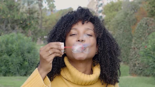 Smiling African American Young Woman Blowing Soap Bubbles in a Park