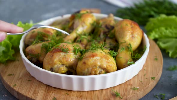 chef checks the readiness of fried chicken drumsticks with chopped herbs, served in white bowl