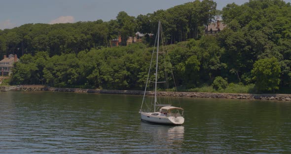 Panning Around a Sail Boat on Harbor and a View of Luxury Mansions Amongst Trees