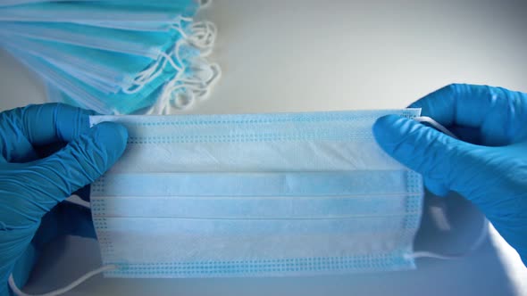 Blue medical gloves holds surgical face mask on blue background. Pandemic concept.