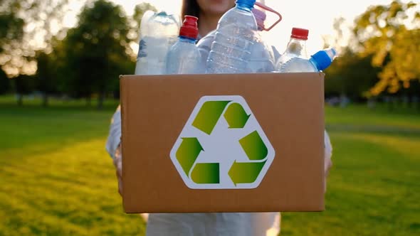 Young unidentified woman holds and hands a box with plastic bottles