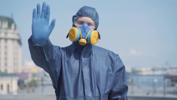 Portrait of Confident Man in Chemical Suit Stretching Hand in Protective Blue Glove To Camera