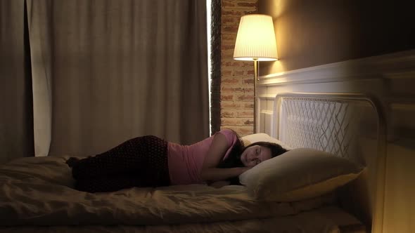 Girl in colored pajamas sleeps in the bedroom on a white bed with night lamp on