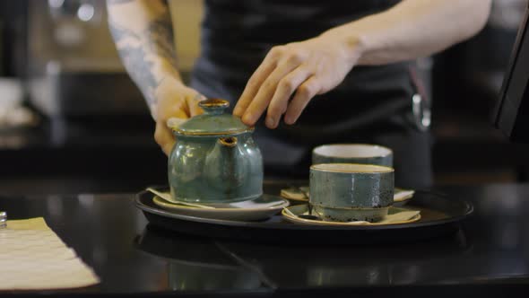 Tattooed Barista Carrying Away Tray with Tea for Two