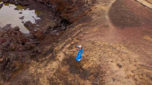 View From the Height of Woman in a Beautiful Blue Dress and Hat Stands on Top of a Mountain in a