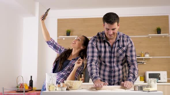 Woman Taking a Selfie in the Kitchen While Man Is Preparing the Dough