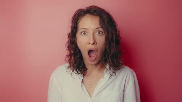 Shocked Woman Face with Opened Mouth and Eyes Looking to Camera on a Pink Wall Background
