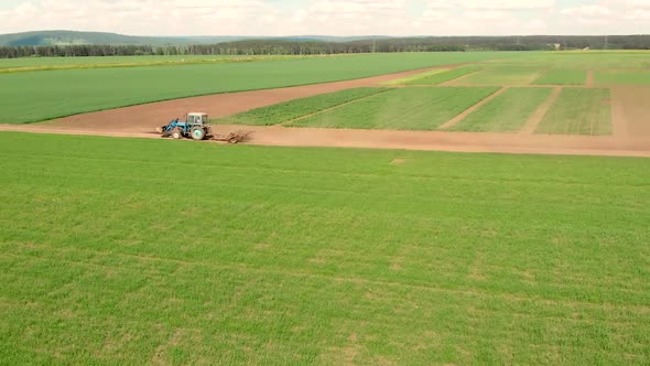 Drone Flying Over Field and Blue Cultivation Tractor Driving on a Ground Road