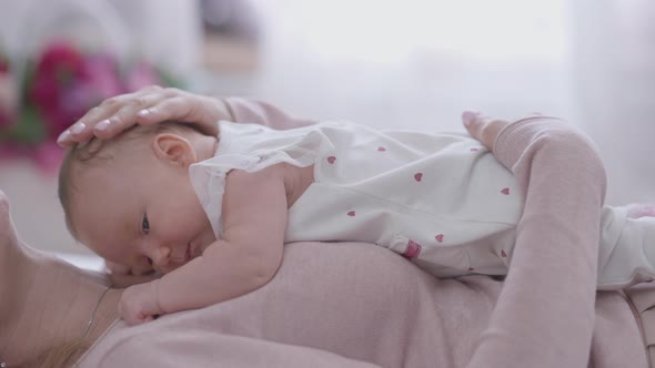 Side View Caucasian Little Baby Girl Lying on Unrecognizable Woman Looking Aside