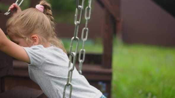 Little Girl Stands on Knees on Wooden Swings on Playground