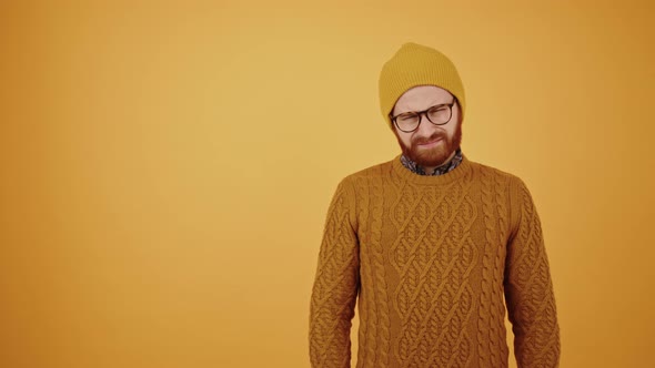 Middleaged Bearded Millennial Man in a Beanie and Warm Yellow Sweater Throwing Hands in the Air Not