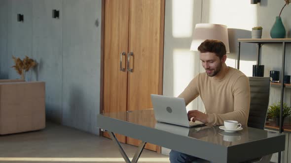 Smiling man typing on laptop at his desk at home office