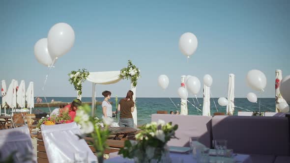 Three Females Decorating Terrace Near Sea with Balloons and Wedding Arch with Flowers in Slowmotion