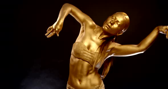 Female Dancer Is Moving in Black Background in Studio, Wriggling Her Golden Body and Hands