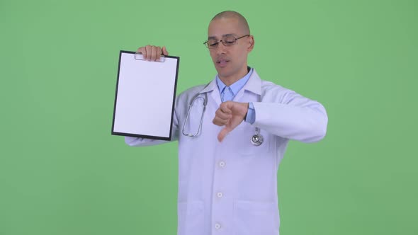 Stressed Bald Multi Ethnic Man Doctor Showing Clipboard and Giving Thumbs Down
