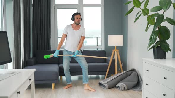 Man in Headphones Does the Cleaning and Imagines Himself a Rock Star Plays the Broom Like a Guitar