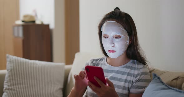 Woman apply face mask and use of mobile phone at home