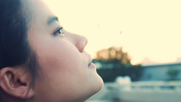 Asian sportswoman keeping eyes closed and breathing fresh air at the park.