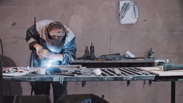 Young Man Worker in Protective Gloves and Helmet Welding Parts of the Metal Detail Together at the