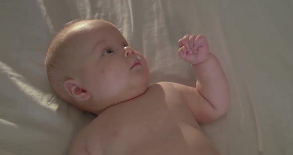 Top Portrait of Naked Newborn Baby Looks at Camera Confusedly